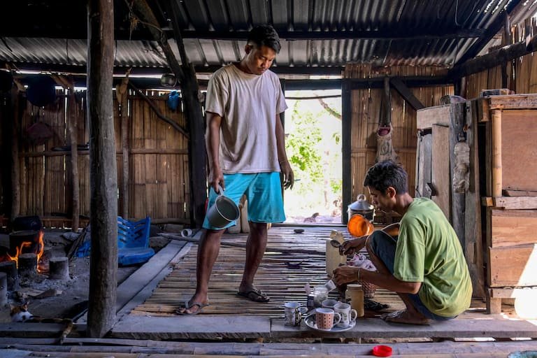 This photo taken on June 23, 2026 shows Umbu Ana Rara (L), a maramba (nobleman), looking on as his ata (slave), Kanisius Kanyali Hambarita, prepares drinks at Tanggedu village in East Sumba, East Nusa Tenggara. Two hours from the tourist beaches of Bali, slavery is alive and well on the Indonesian island of Sumba, where people are still being born into bondage. Eight of out 10 of Sumba's population of 685,000 people are Christian but its older "marapu" belief system, that blends animism and ancestor worship, has deep roots. It divides society into three castes, "the nobles, called 'maramba' -- often large landowners -- ordinary people called 'kabihu' and the slaves/servants, the atas," said rights activist Martha Hebi, author of several studies on the subject. (Photo by BAY ISMOYO / AFP) / To go with Indonesia-Sumba-slavery, SPECIAL REPORT by Eric Bernaudeau