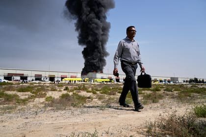 Un hombre se aleja tras observar una columna de humo negro que se eleva desde un depósito en la zona industrial de la ciudad de Sharjah, Emiratos Árabes Unidos