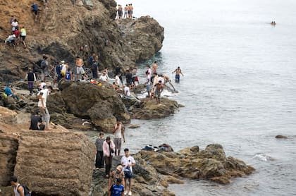 Unas personas permanecen en la orilla mientras intentan cruzar desde la localidad marroquí de Fnideq, en el norte, hasta el enclave español de Ceuta