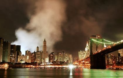 El humo de los restos humeantes del World Trade Center ondea sobre el horizonte del Bajo Manhattan, recortando la silueta del edificio Woolworth, en el centro, la madrugada del domingo 16 de septiembre de 2001