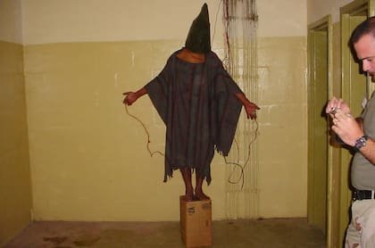 Esta imagen obtenida por The Associated Press muestra a un detenido no identificado de pie sobre una caja con una bolsa en la cabeza y cables atados a él en la prisión de Abu Ghraib en Bagdad, Irak, a finales de 2003