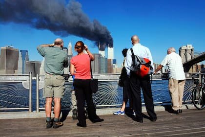 Los personas en el paseo marítimo de Brooklyn, Nueva York, miran a través del East River hacia las torres del World Trade Center en llamas