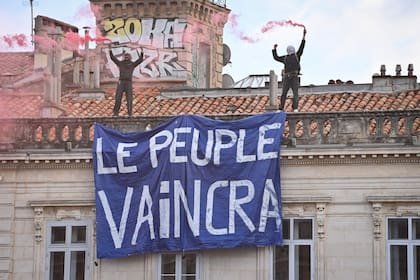 Manifestantes sostienen una pancarta en la que se lee «El pueblo vencerá» mientras permanecen sobre el tejado de un edificio durante una protesta contra el «alto costo de la vida» en Montpellier, en el sur de Francia